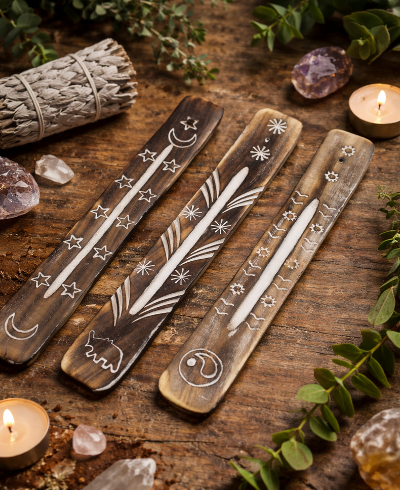 Drie gebeeldhouwde houten wierookhouders met sterren, manen en symbolen op een houten tafel met kristallen en kaarsen.