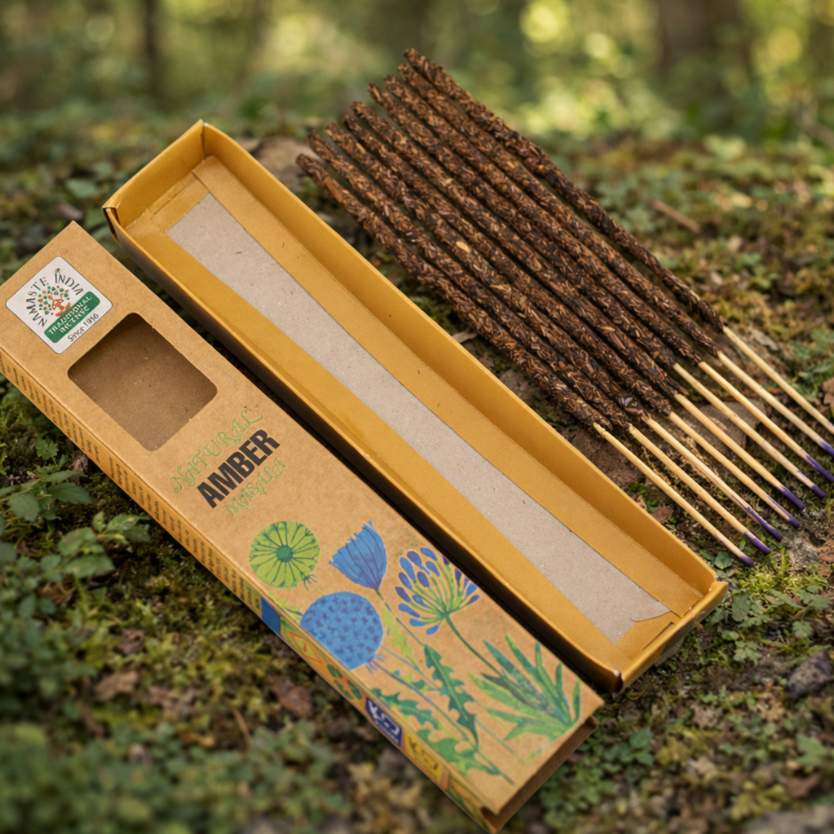 Een doos met wierookstokjes ligt open op de met mos bedekte grond, omringd door wilde bloemen en andere planten.