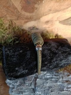 Een groene en zilveren armband rust op een donkere rots met mos op de achtergrond.