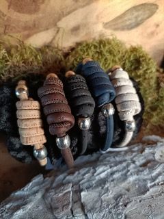 Een opgerold, lichtbruin kleiobject met metalen uiteinden, geplaatst tegen een achtergrond van rotsen en mos.