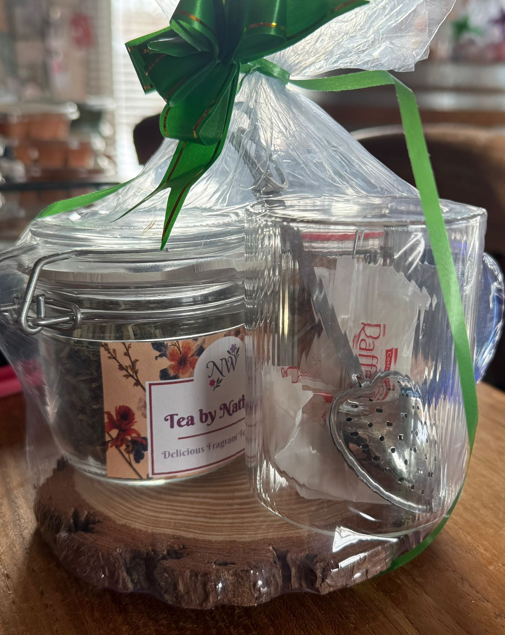 Cadeauset met thee: pot losse thee, transparante mok met theefilter, vastgebonden met een groen lint, op een houten schijfje.