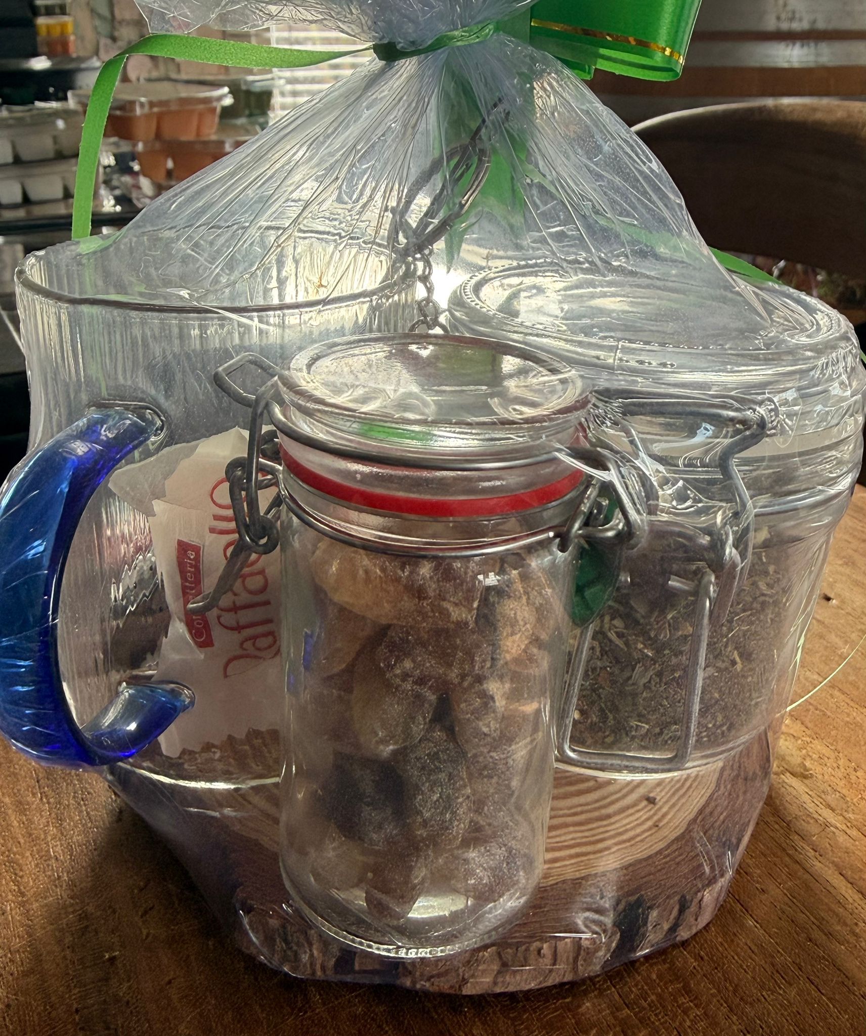 Cadeauset met thee: pot losse thee, transparante mok met theefilter, vastgebonden met een groen lint, op een houten schijfje.