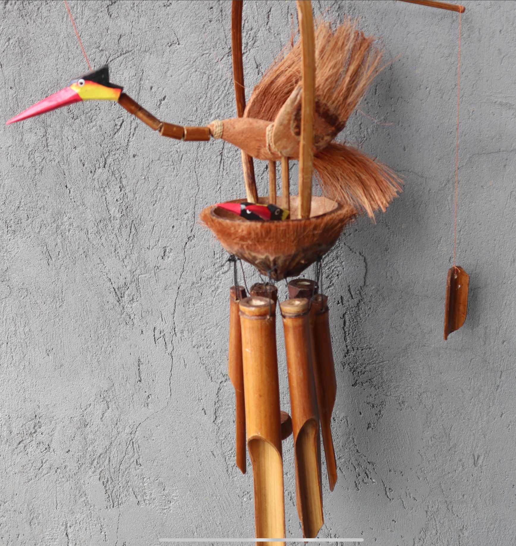 Houten windgong, gemaakt van kokosnootschaal en bamboe. Rode snavel, bruin lichaam, hangend voor een bakstenen achtergrond.