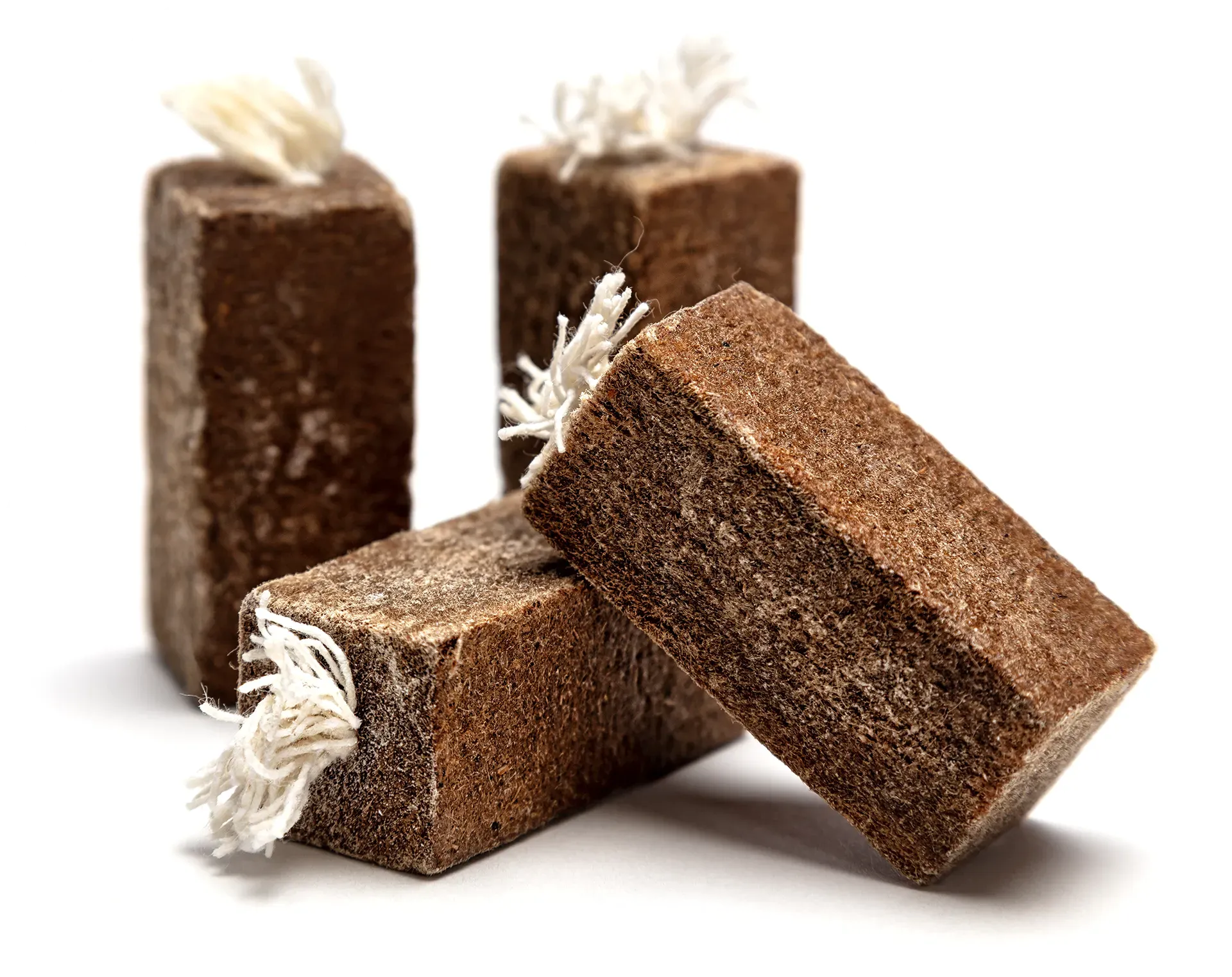 Three brown firestarter with cotton wicks attached to them are stacked on top of each other on a white background.