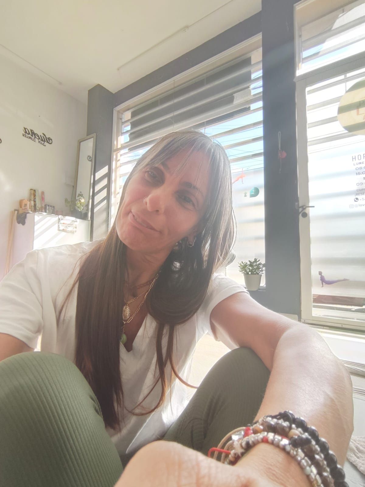 Una persona con cabello largo, liso y castaño posa en el interior, vistiendo una camisa blanca