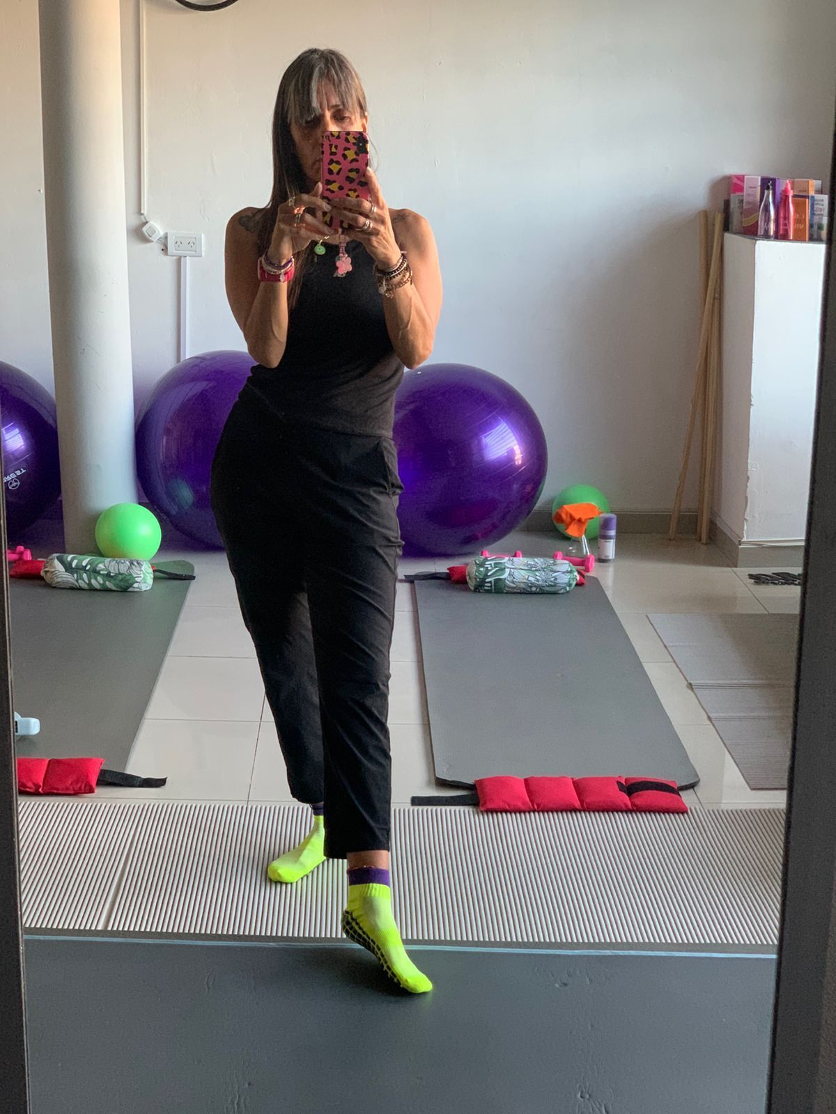 Una persona vestida con una camiseta de tirantes negra y pantalones se toma una selfie frente al espejo en un gimnasio