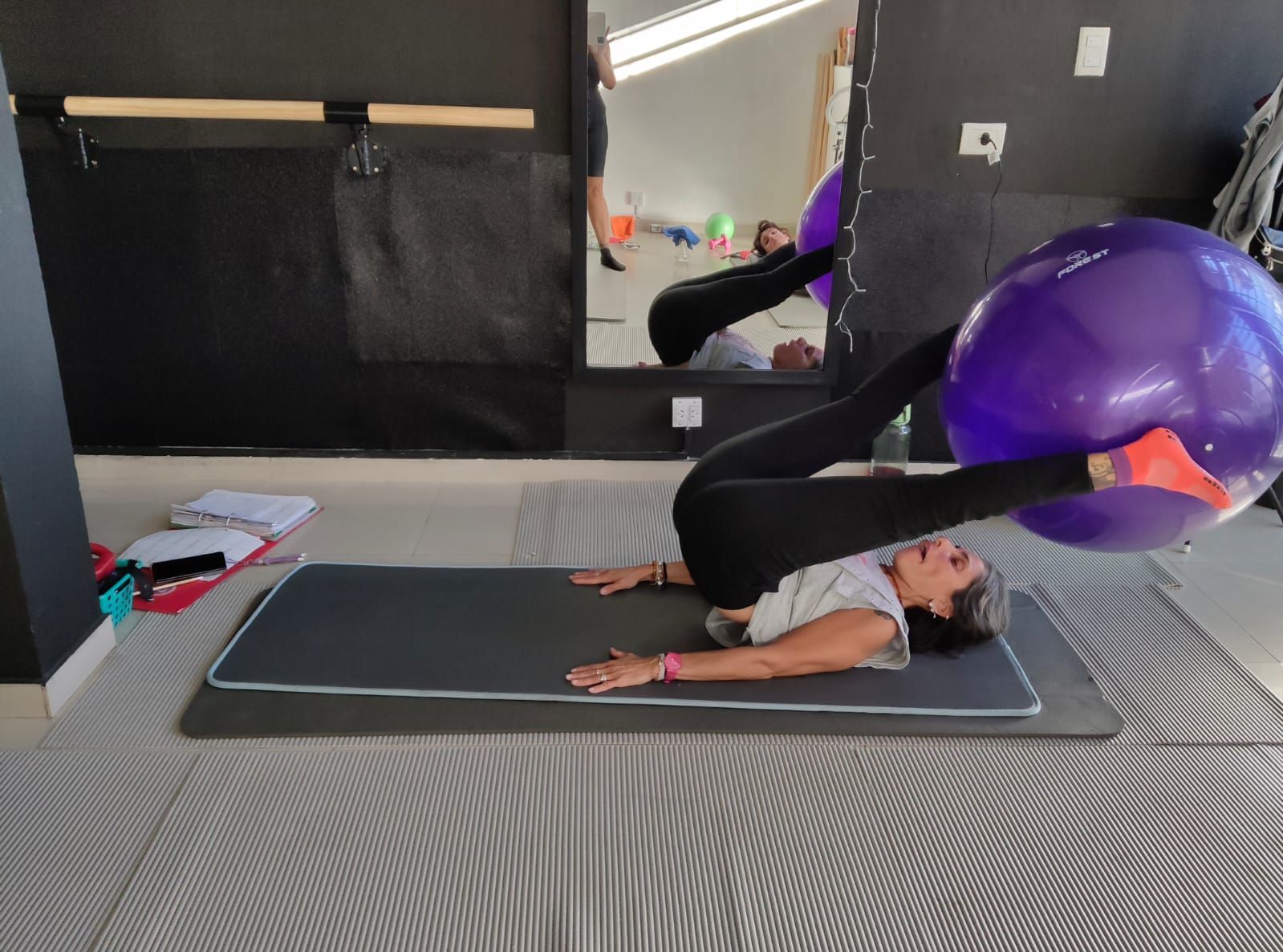 Una persona yace sobre una colchoneta en el suelo, levantando las piernas para sujetar una gran pelota de ejercicio