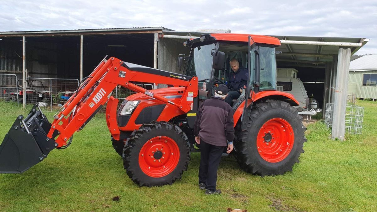 A Man is Standing Next to a Red Tractor in a Grassy Field — Stockers & Partridge In Maitland, NSW