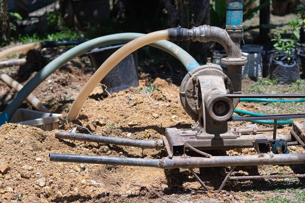 A Water Pump is Sitting in the Dirt With Hose Attached to It — Stockers & Partridge In Dungog, NSW