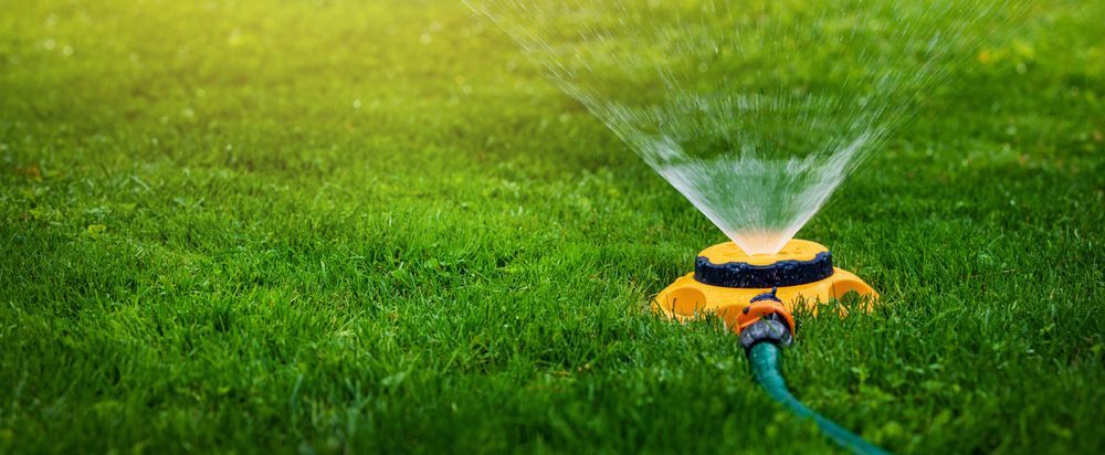 A Yellow Sprinkler is Spraying Water on a Lush Green Lawn — Stockers & Partridge In Paterson, NSW