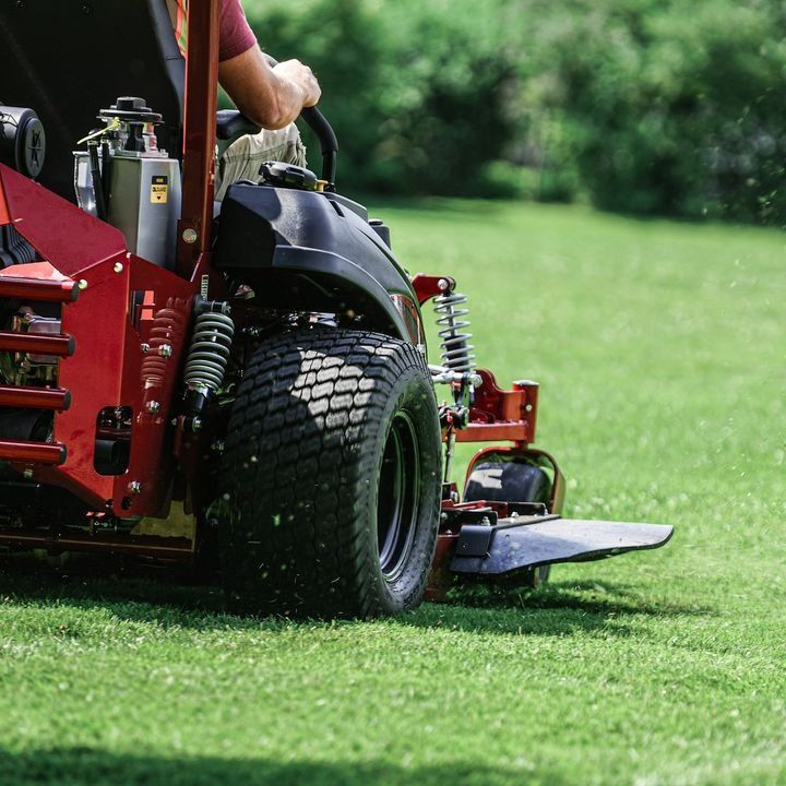 A Red Lawn Mower is Cutting a Lush Green Field of Grass — Stockers & Partridge In Paterson, NSW