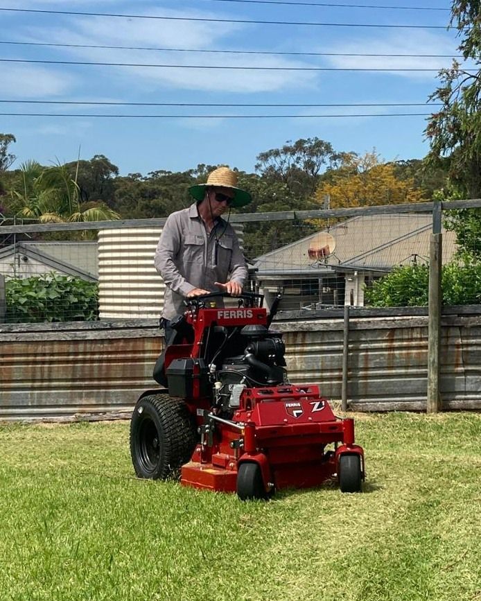 A Man is Riding a Red Lawn Mower on a Lush Green Lawn — Stockers & Partridge In Paterson, NSW