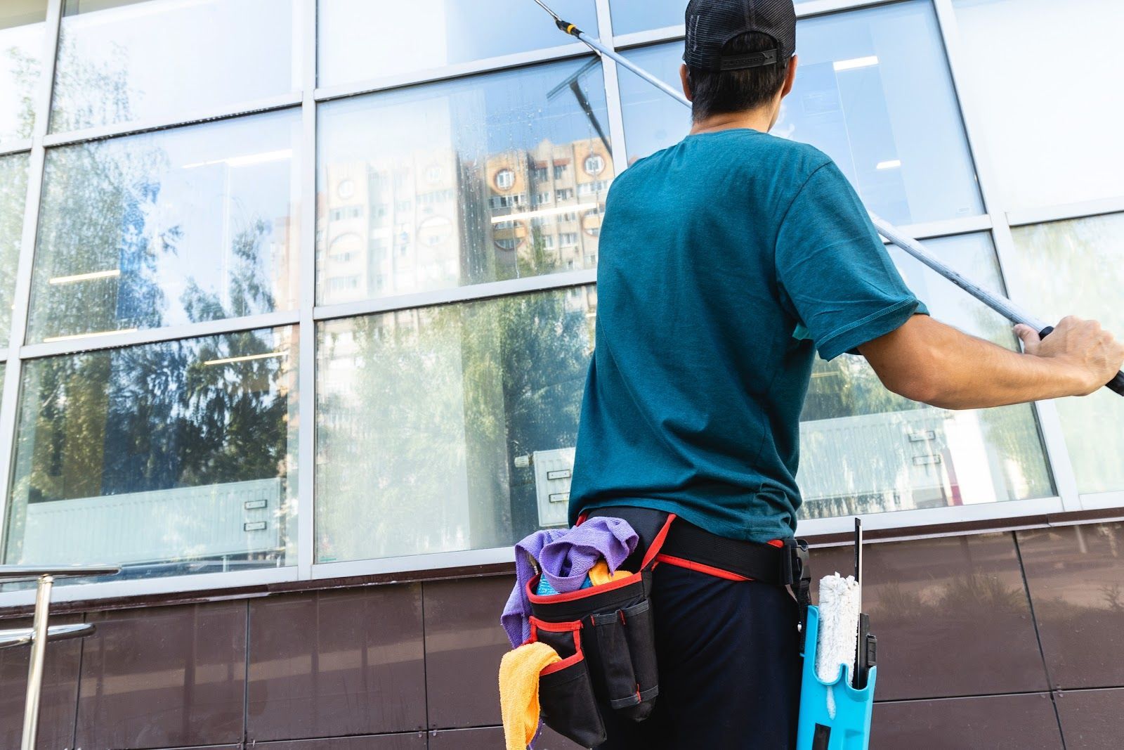 Window washer cleaning a large window with a squeegee, wearing a tool belt.