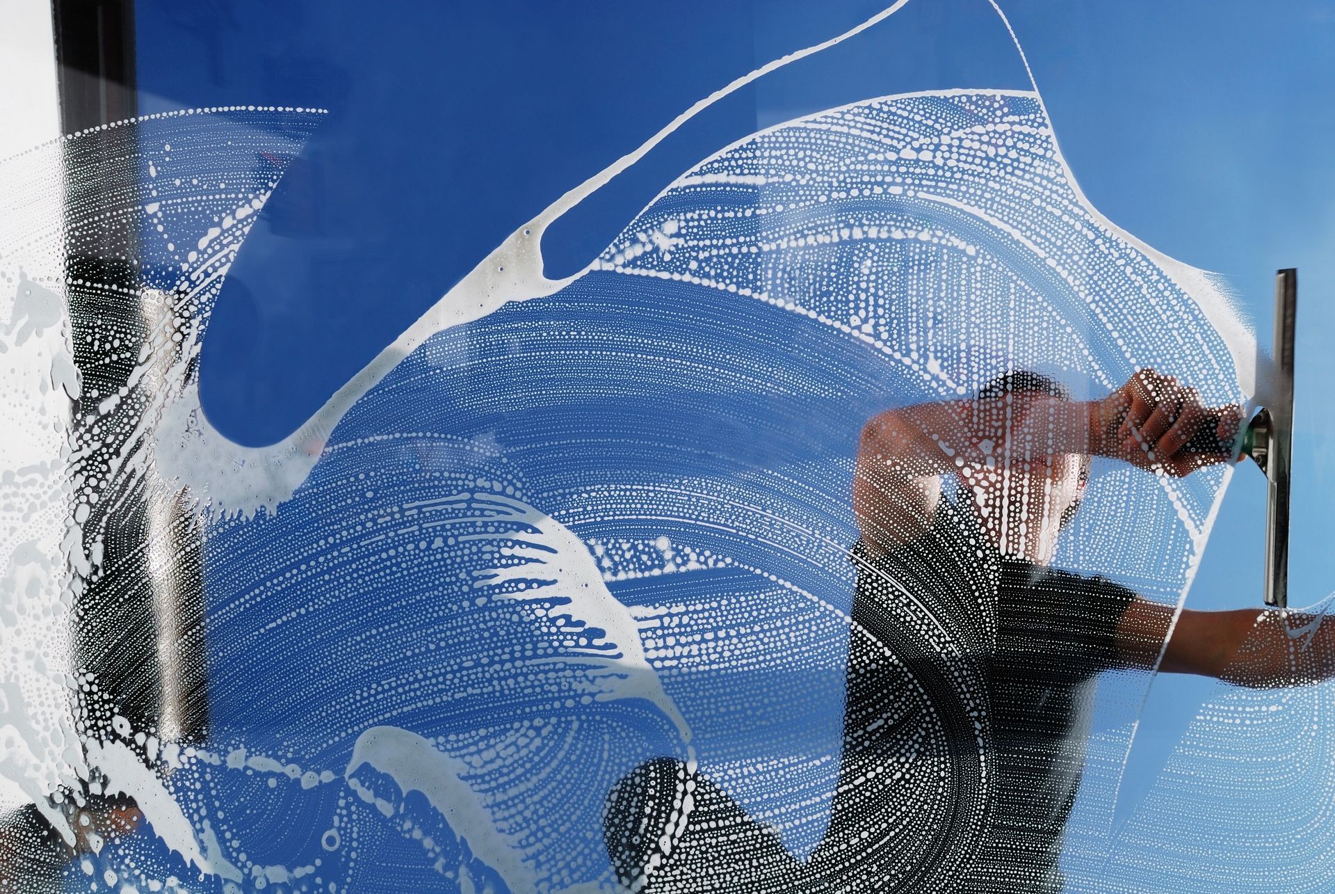 A person squeegeeing soapy water off a large blue window, creating a clean streak; outdoors.