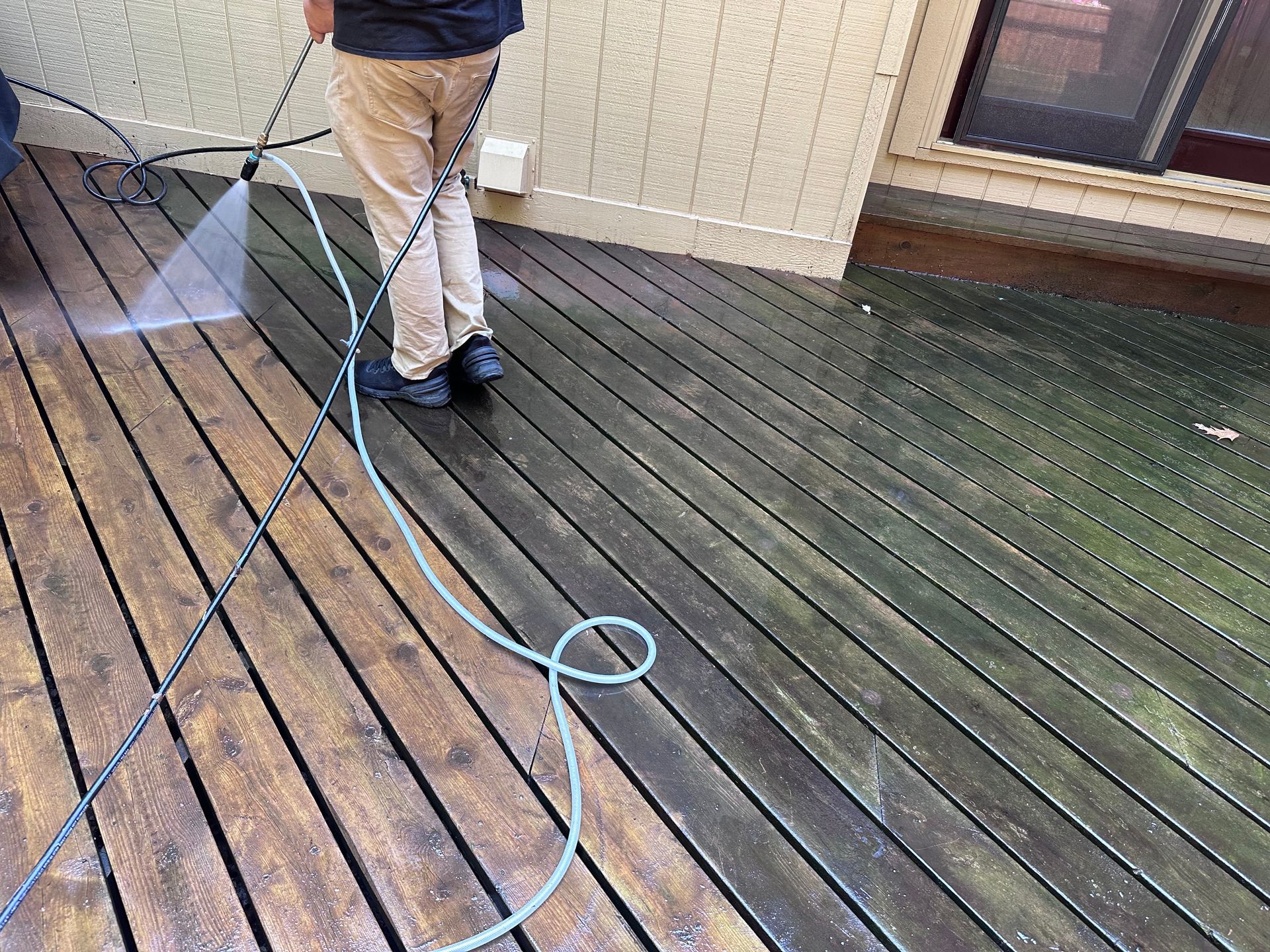 A person is cleaning a wooden deck with a pressure washer.