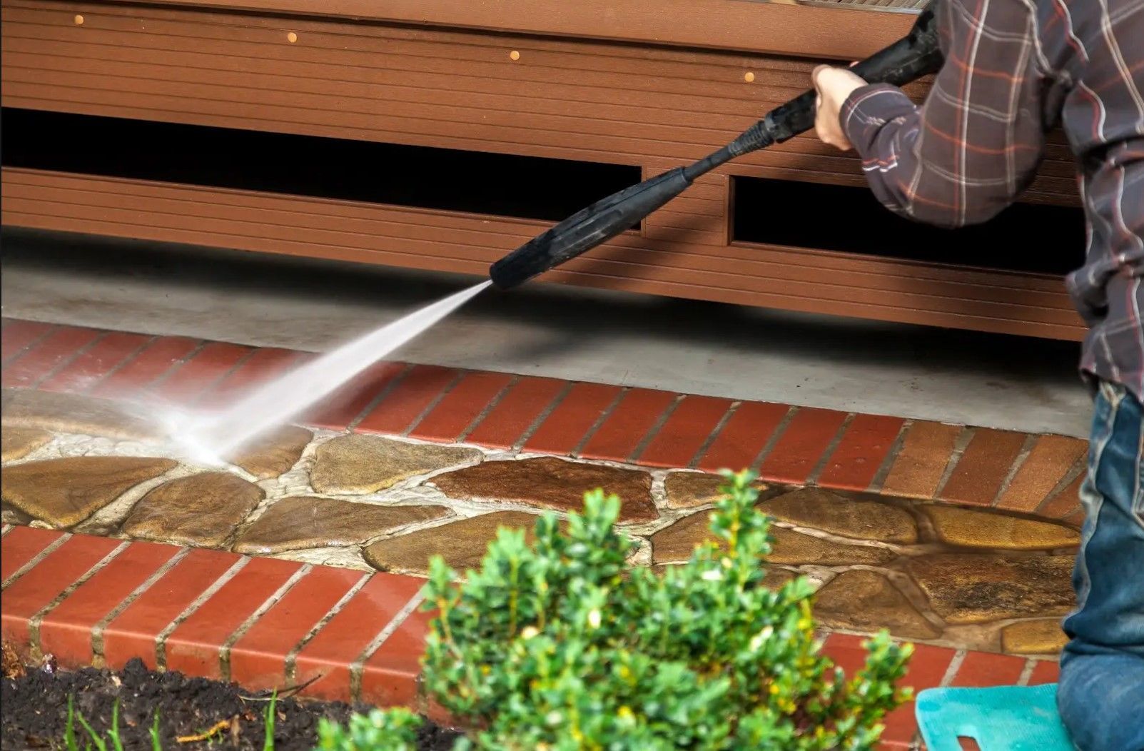 A man is using a high pressure washer to clean a brick walkway.