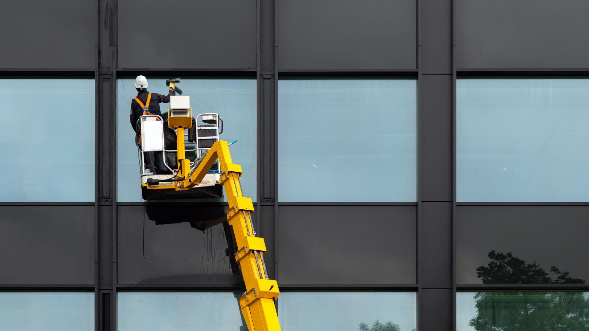 A man is cleaning the windows of a building with a crane.