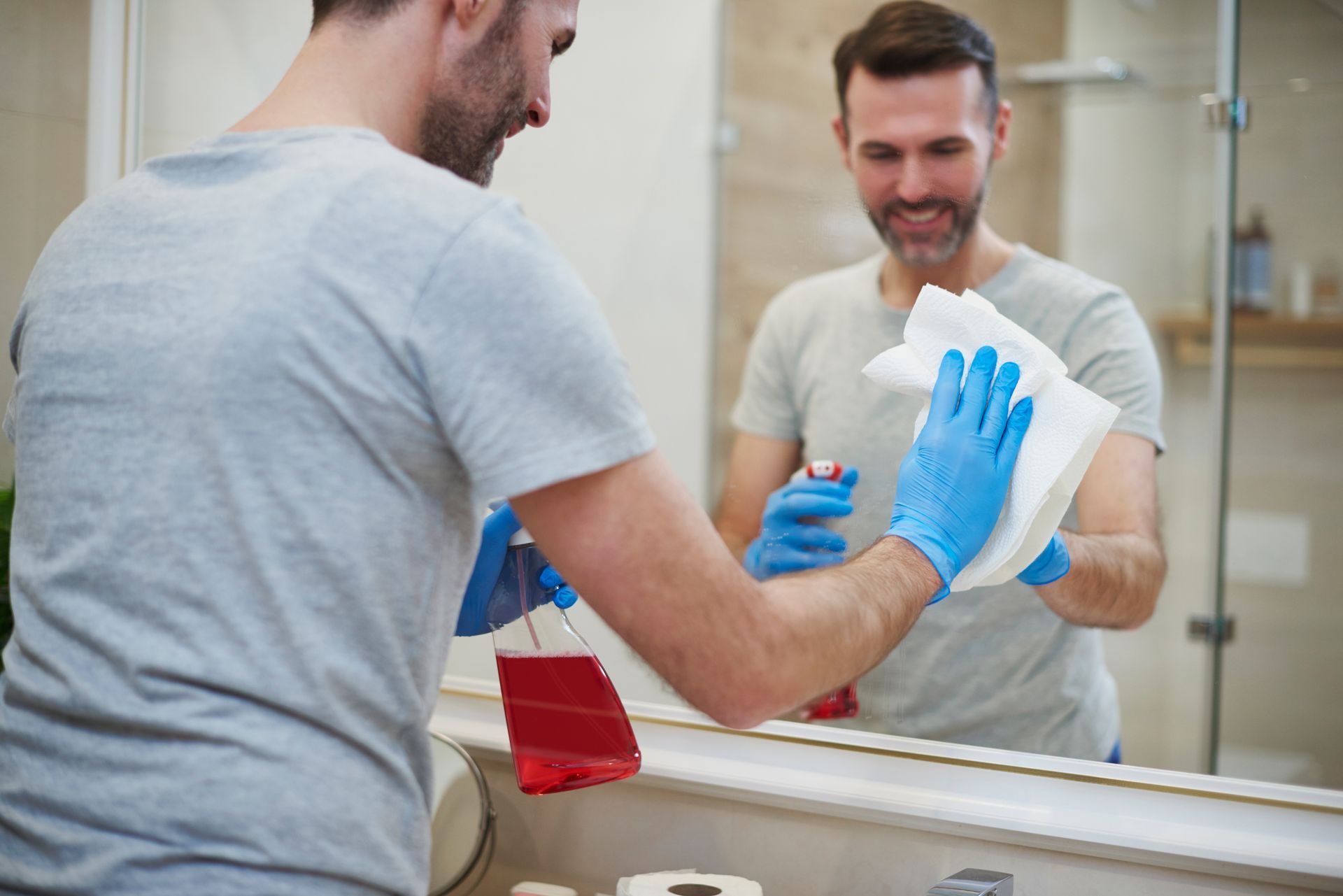 A man is cleaning a bathroom mirror with a towel.