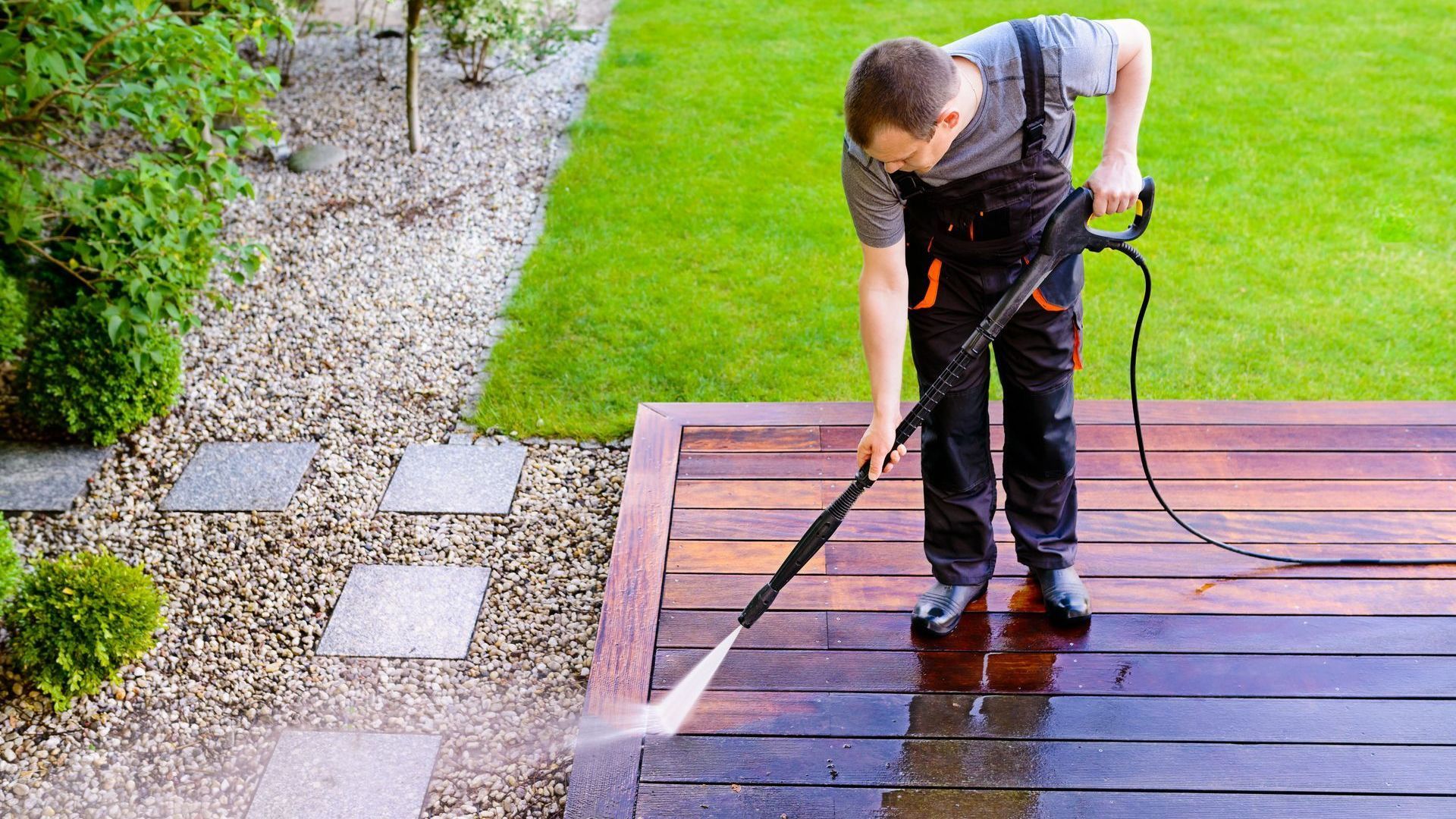 A man is using a high pressure washer to clean a wooden deck.