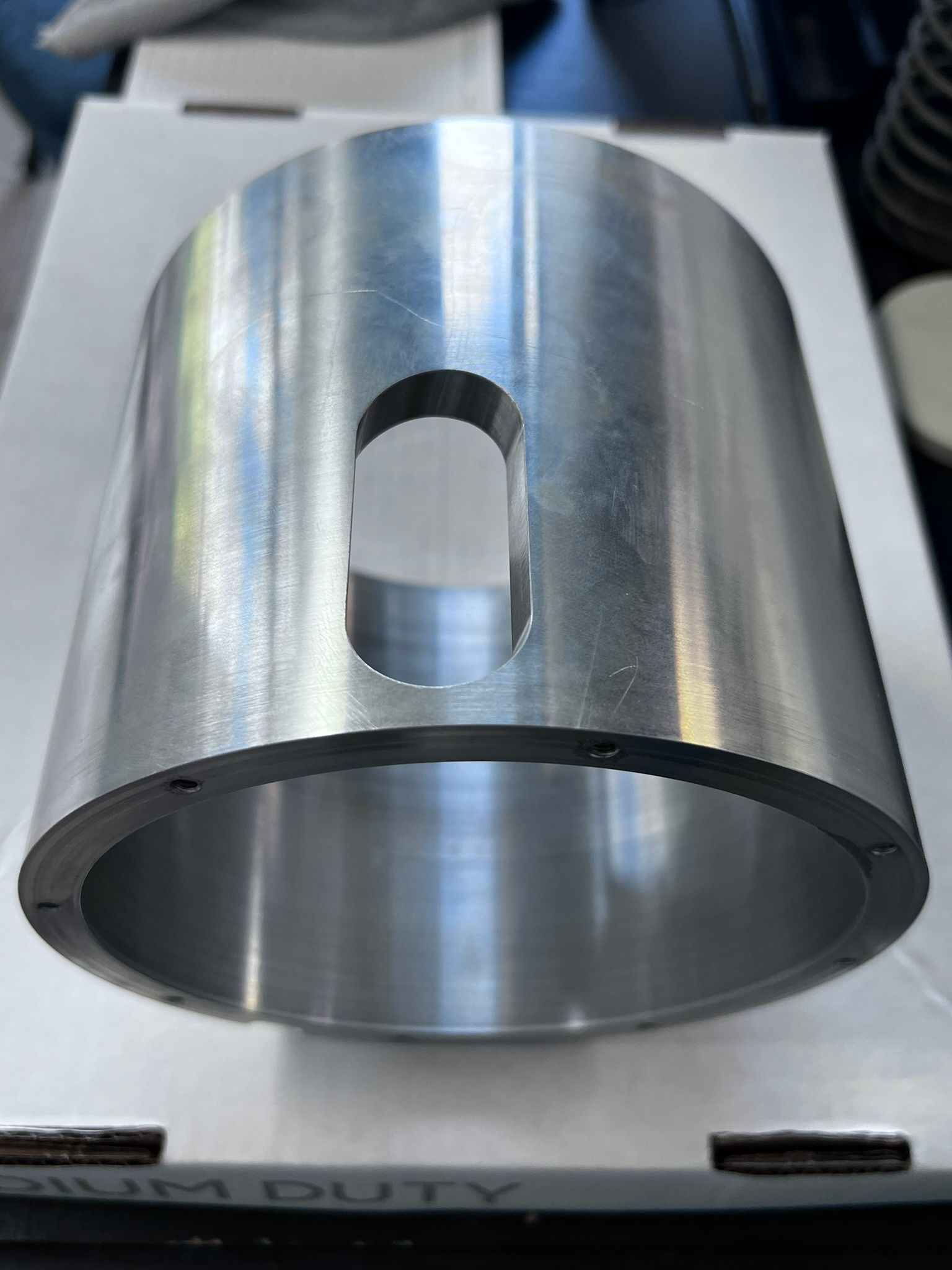 A metal cylinder with a hole in the middle is sitting on top of a cardboard box.