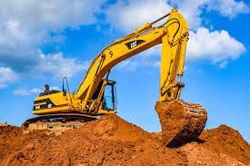 Excavator loading dirt into dump trailer during trench work
