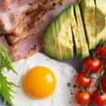 A plate of food with eggs , bacon , avocado and tomatoes.