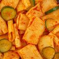 A close up of a pile of pasta with cucumbers and sauce.