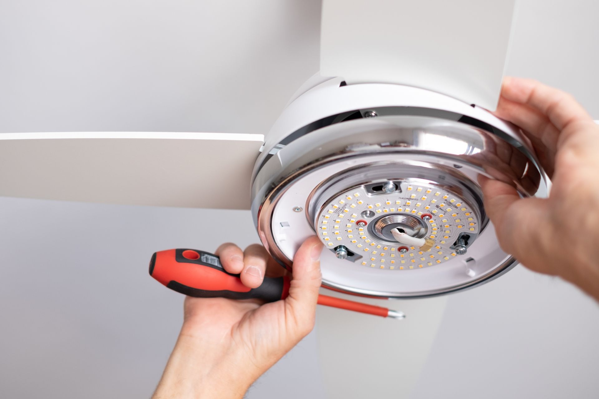 A person is fixing a ceiling fan with a screwdriver.