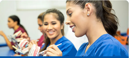 A group of female dental assistants are sitting at a table in a dental office.