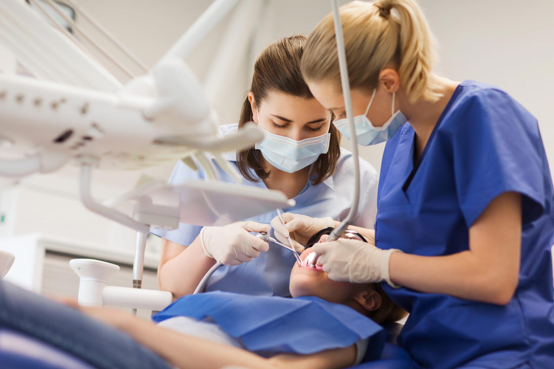 Two female dentists are examining a patient 's teeth in a dental office.