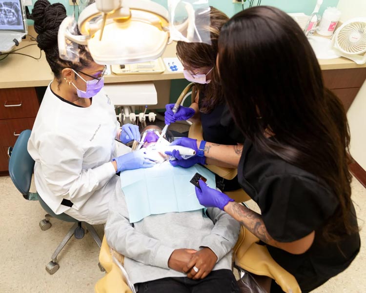 A woman is getting her teeth examined by two dentists