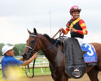 Jockey on a brown racehorse being led by a handler, wearing red-and-black silks and saddlecloth 3.