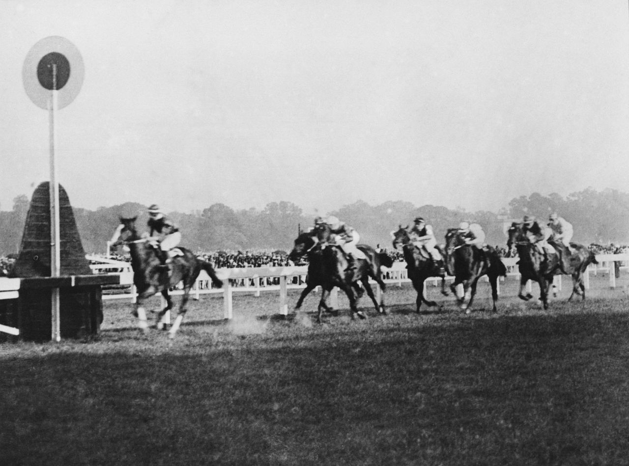 Horse race with jockeys galloping past the finish marker on a dirt track