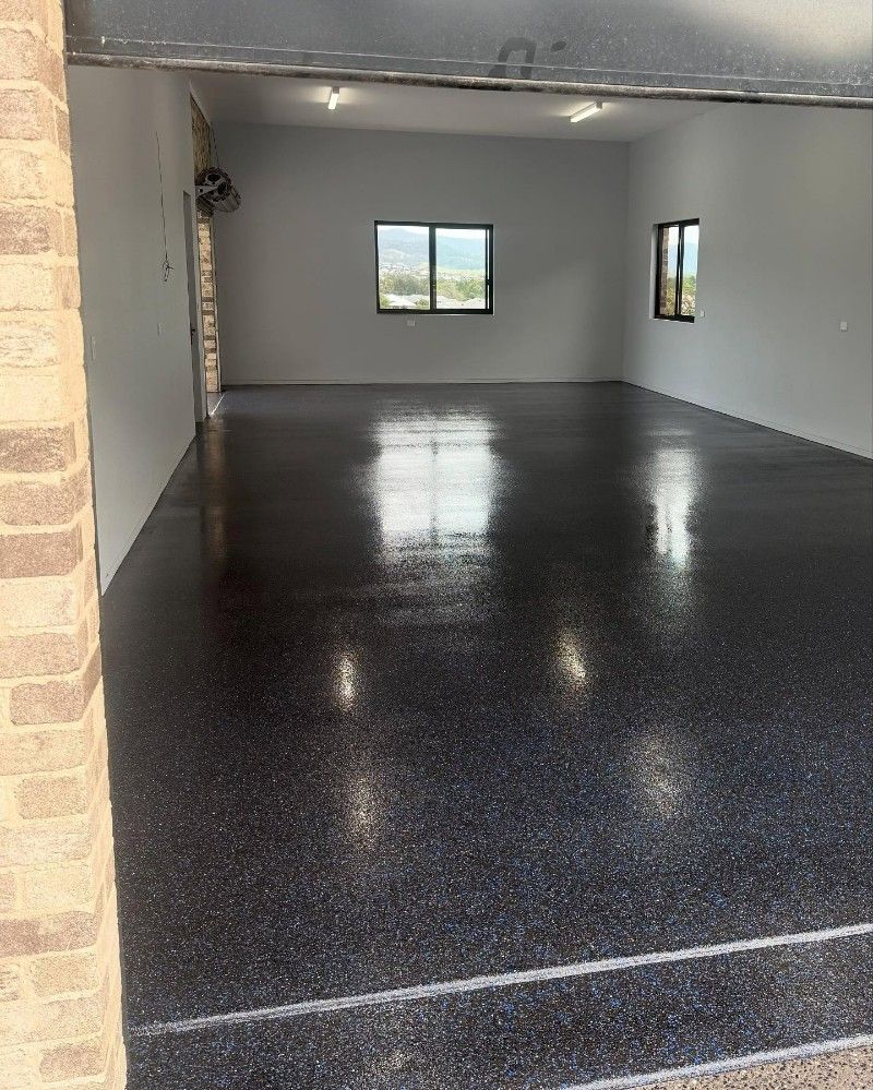 A Large Empty Garage With a Black Floor and White Walls — Premier Epoxy Flooring Wollongong in Wollongong, NSW