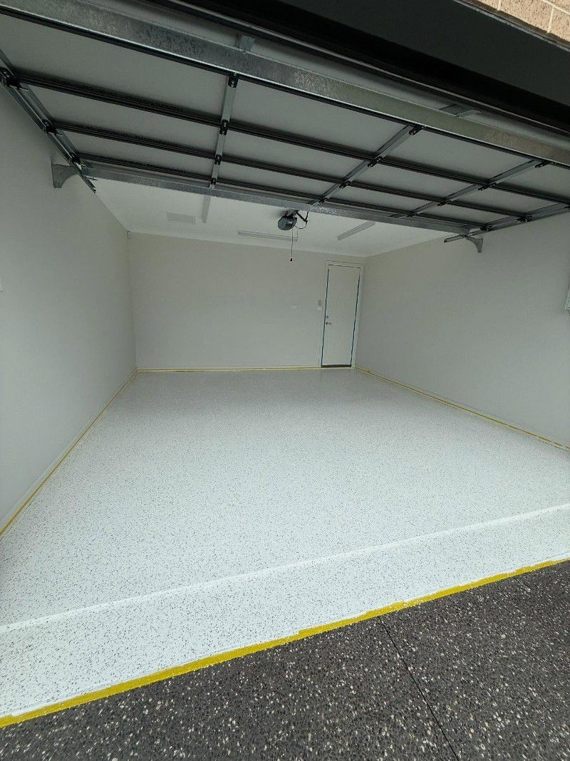 An Empty Garage With a Garage Door Open and a White Floor — Premier Epoxy Flooring Wollongong in Wollongong, NSW