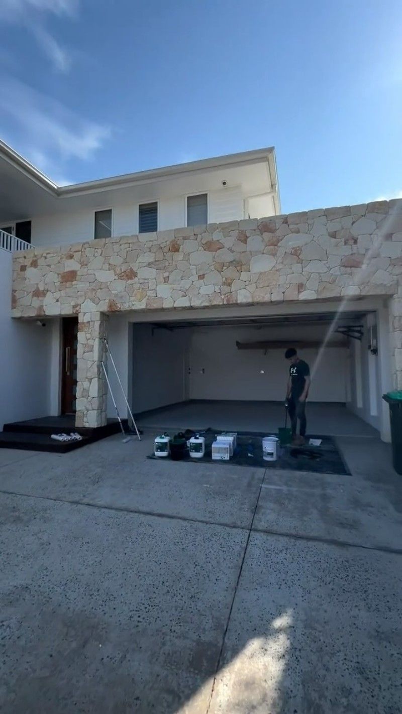 A Man is Painting the Side of a House in a Driveway — Premier Epoxy Flooring Wollongong in Wollongong, NSW
