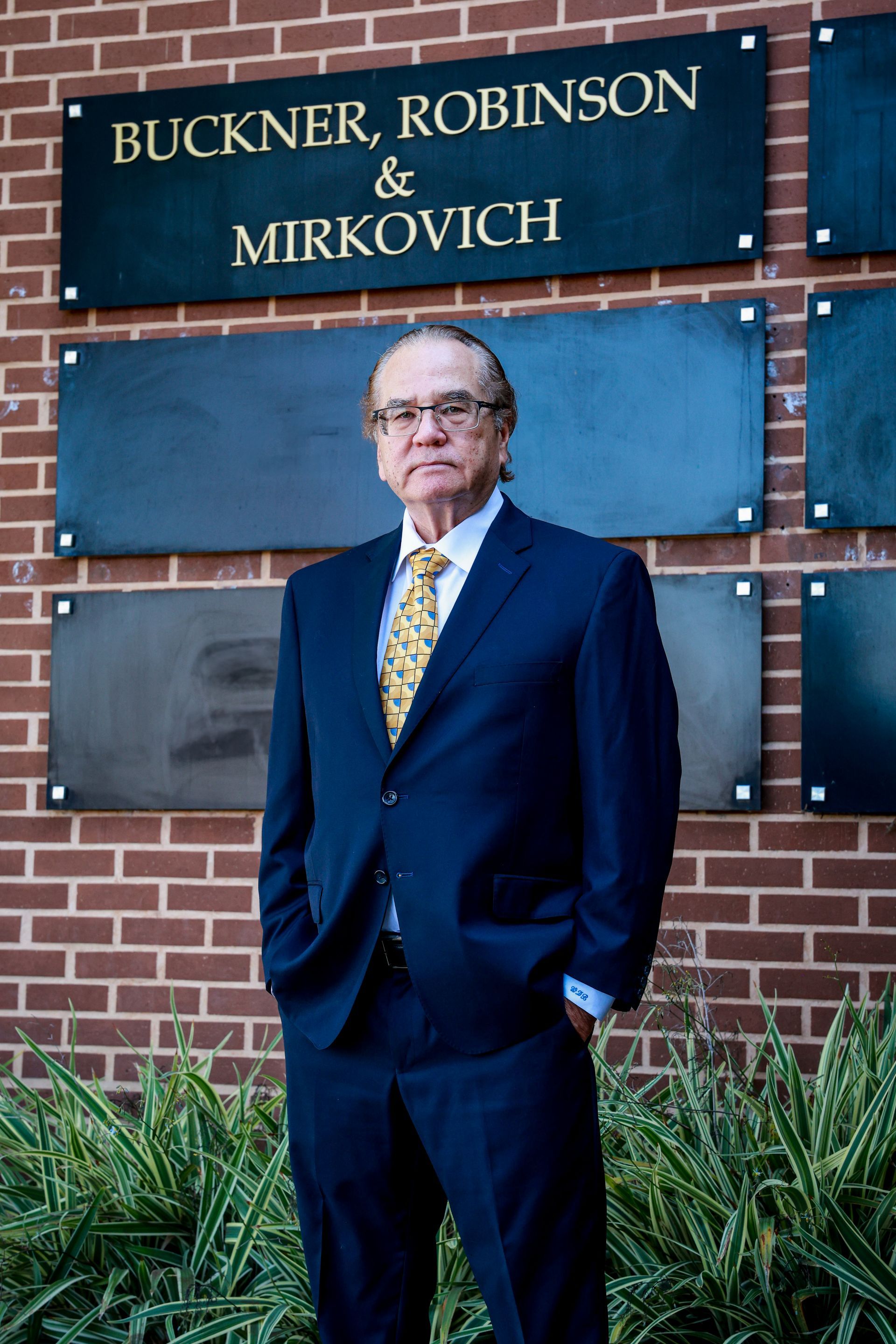 Man in a suit stands in front of a law firm sign on a brick building.