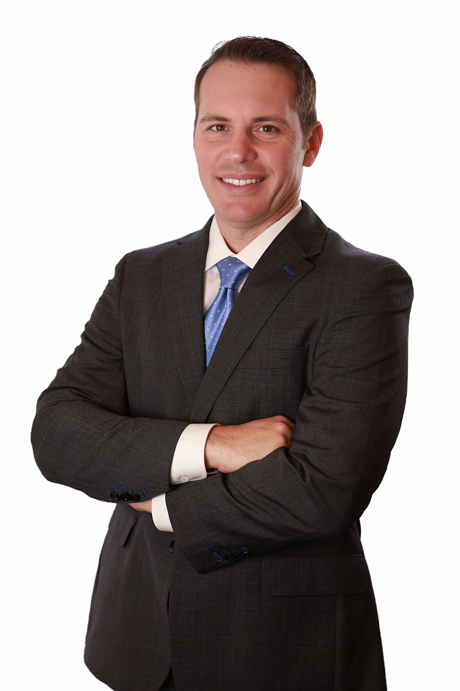 Man in a suit smiles, arms crossed. Dark suit, blue tie, white background.