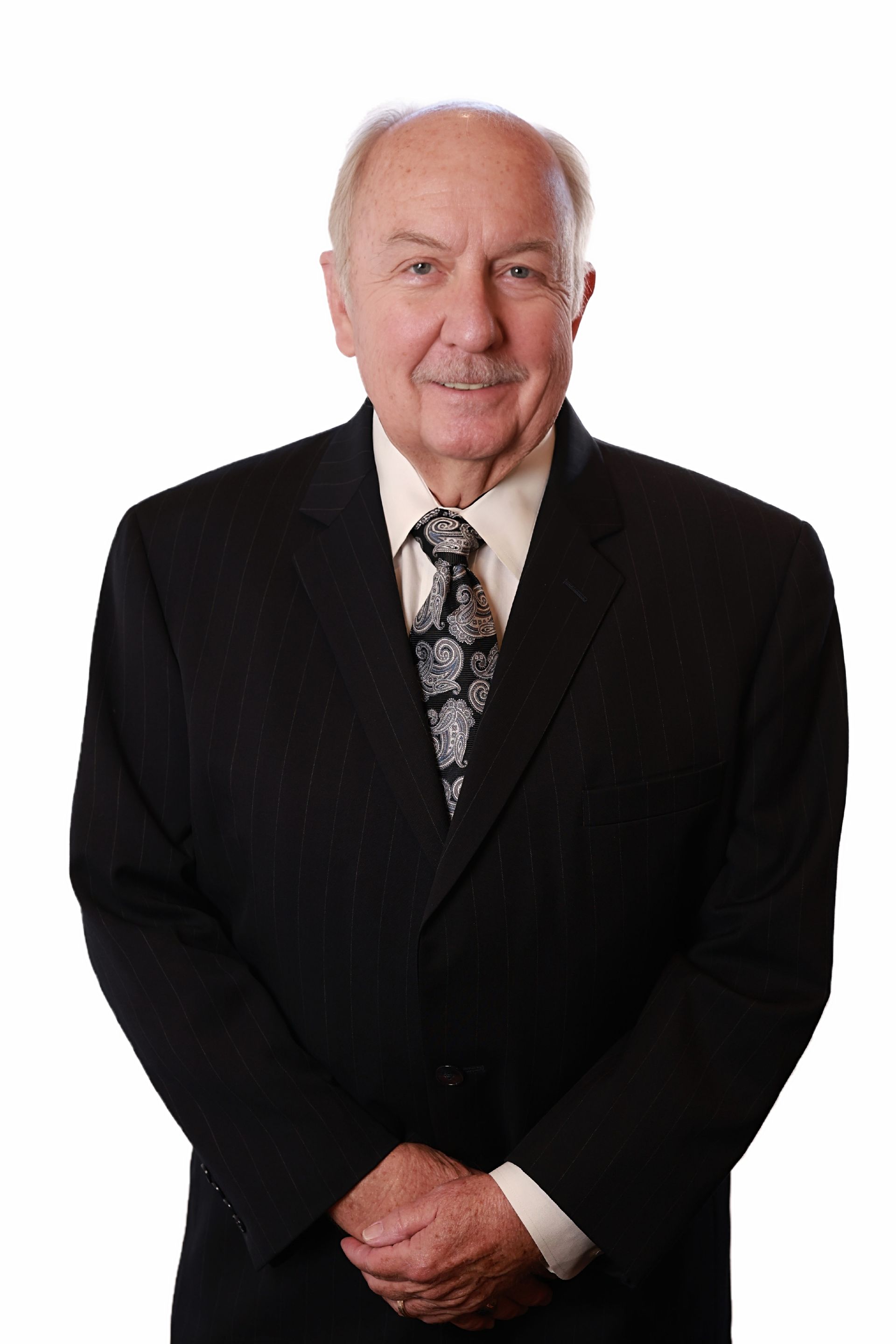 Man in a black suit, standing and smiling, against a white background.