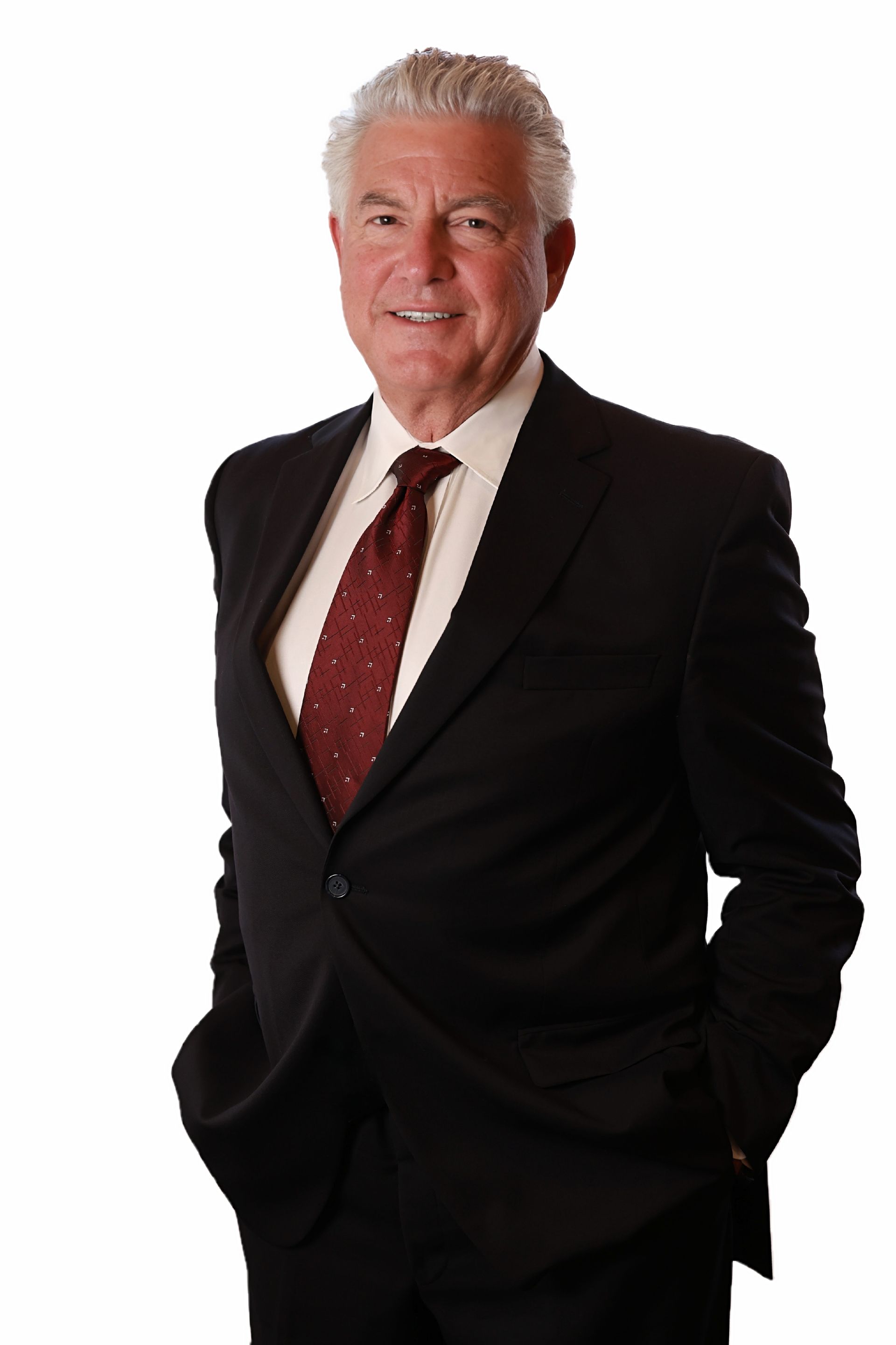 Man in a suit smiles, hands in pockets, against a white background.