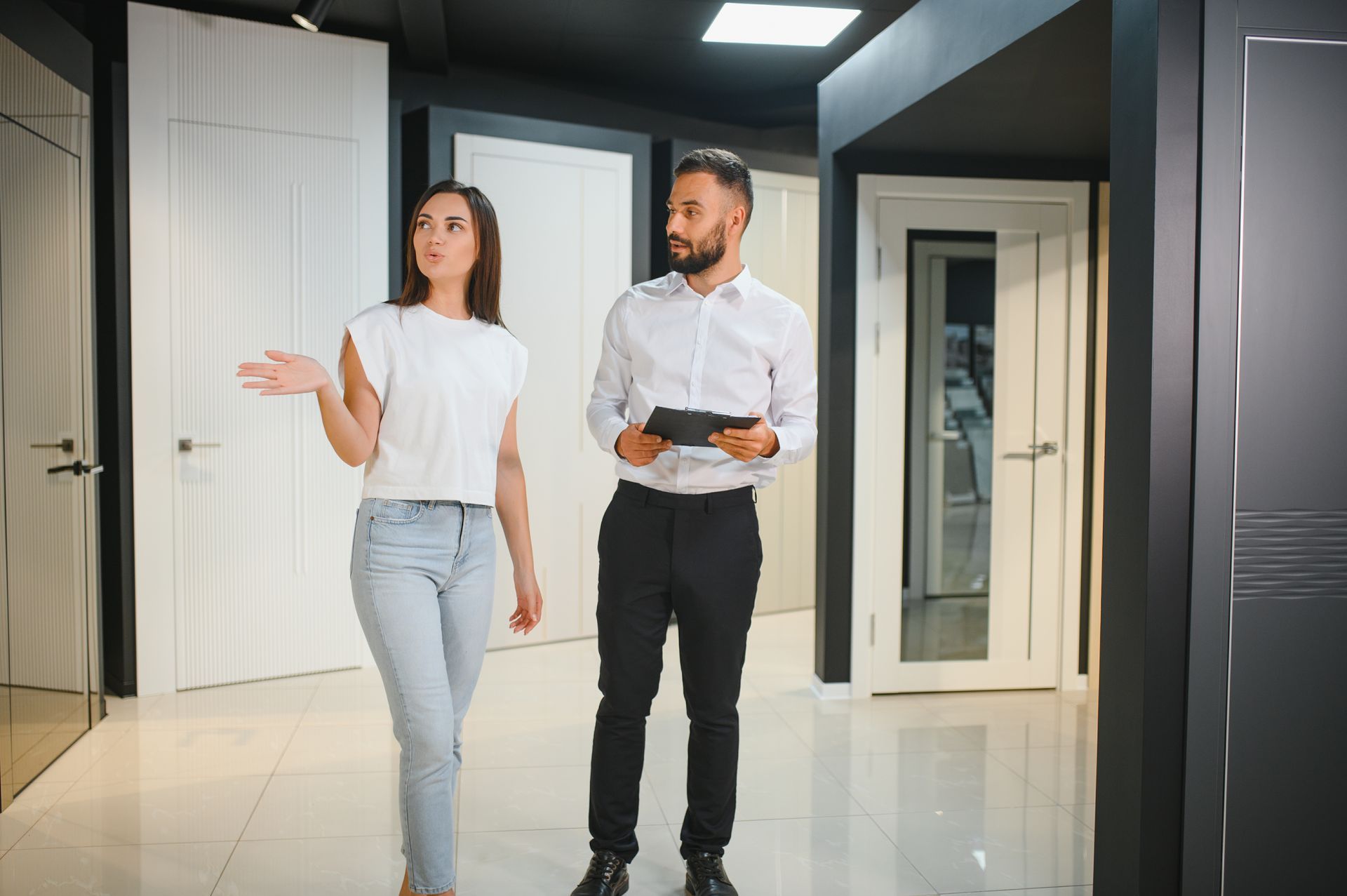 Woman gesturing, looking at doors with a man holding a tablet in a showroom.