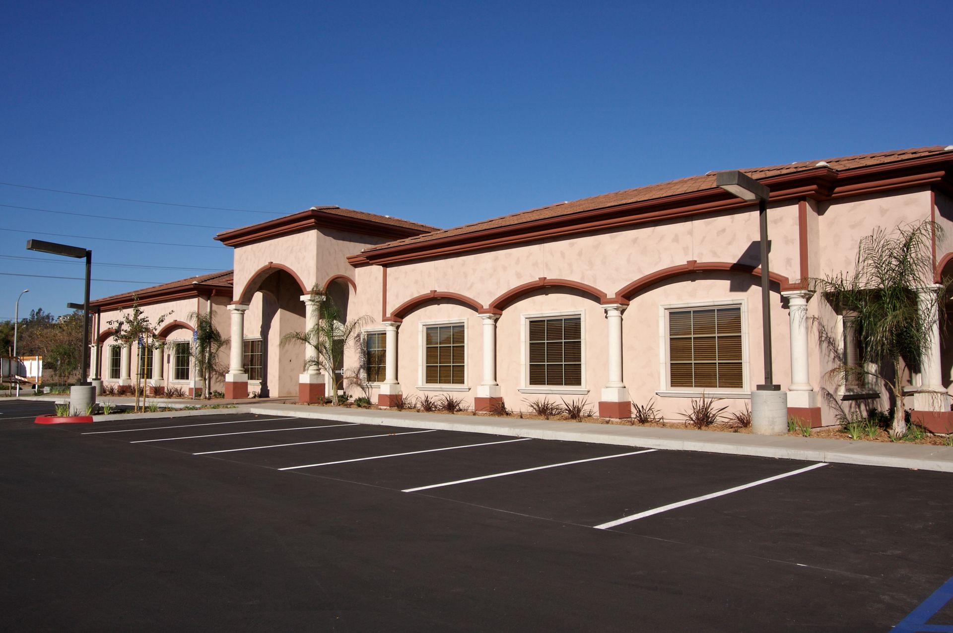Building with arches, brown roof, and parking lot under a blue sky.