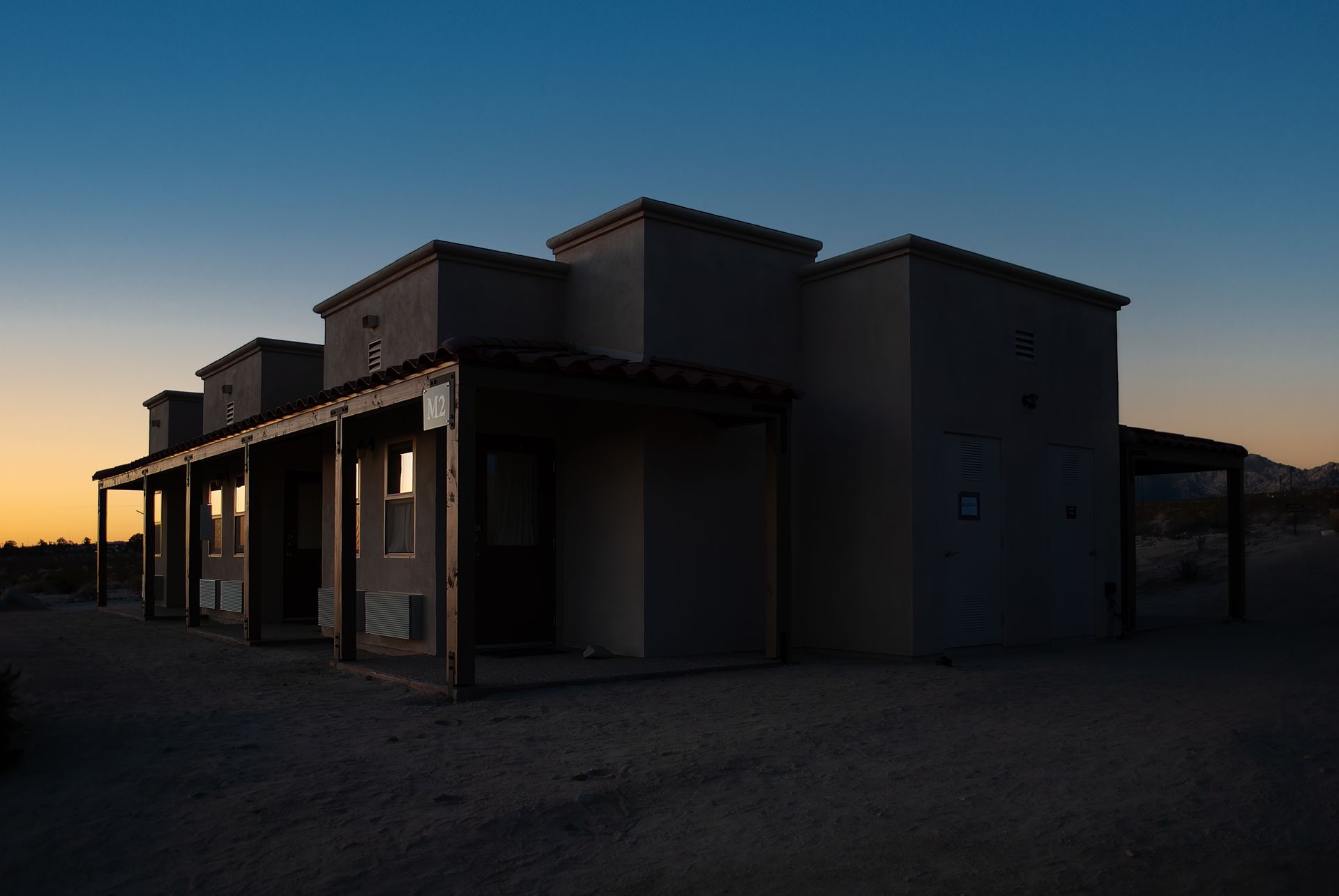 Adobe-style building at dusk with a covered porch and an orange and blue sky.