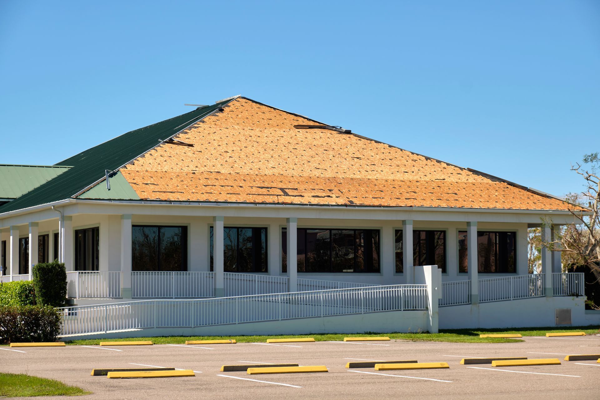 White building with damaged roof and parking lot.