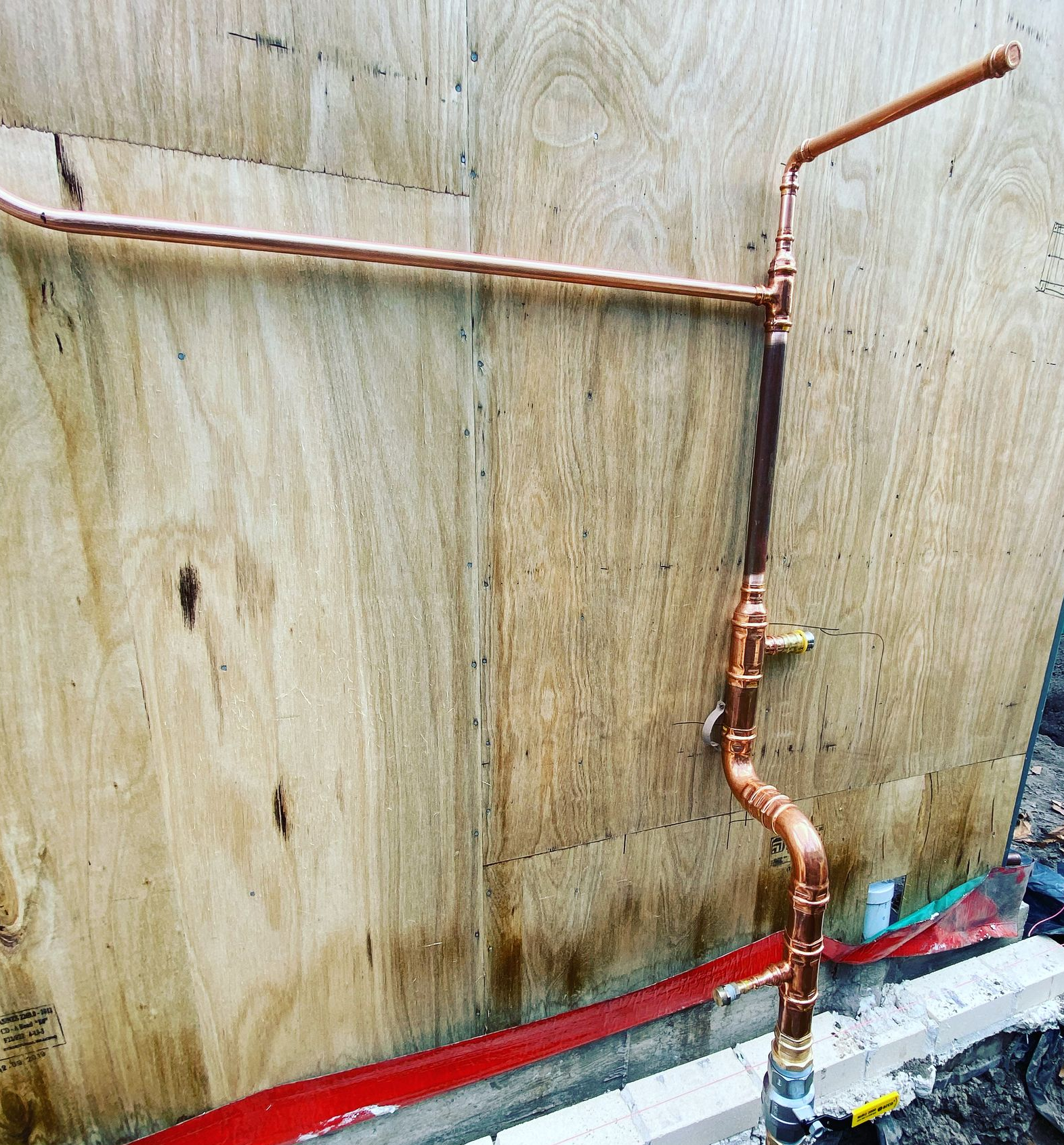 Copper pipes installed on a wooden wall, with a straight horizontal run and vertical sections.