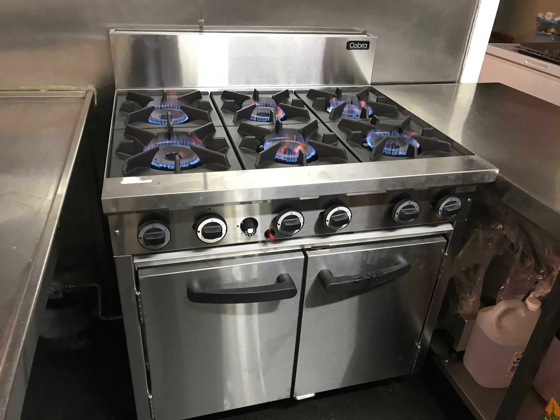 Stainless steel commercial gas range with six burners lit, and two oven doors.