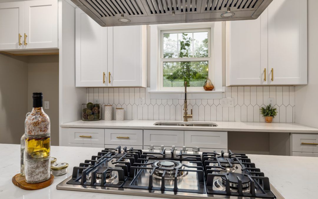 White kitchen with gas stove on island, cabinets, and window.