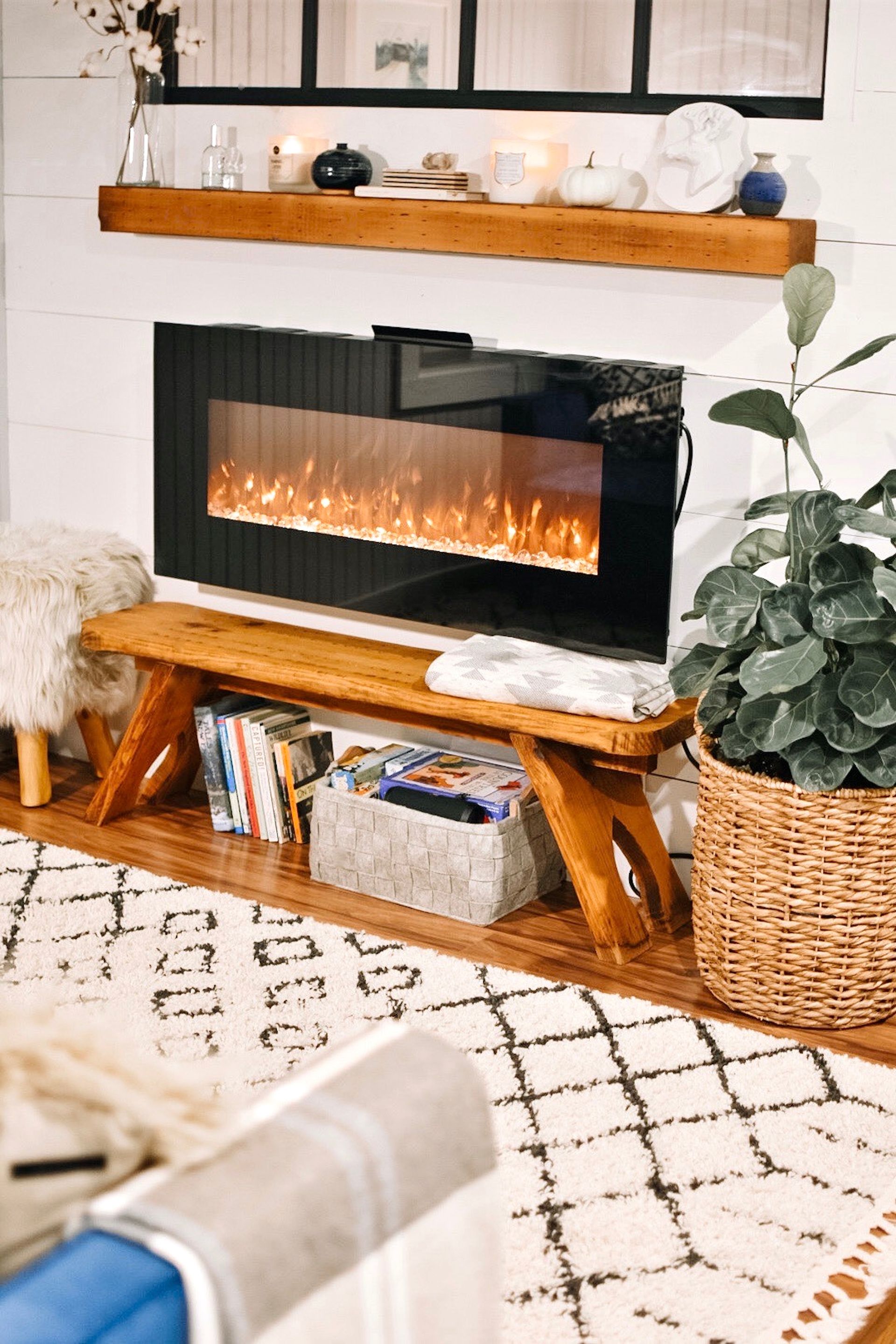 Fireplace with a glowing fire, books, and plants on a wooden bench in a cozy living room.