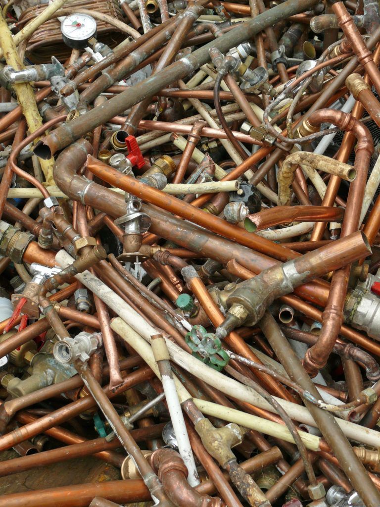 Pile of copper pipes and fittings, some with attached valves and insulation, in various sizes and shapes.