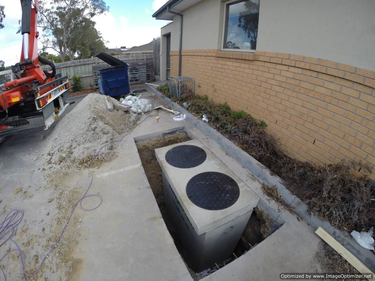 Concrete septic tank being installed next to a brick house. A truck crane is visible on the left.